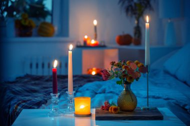 Vazoda sonbahar kasımpatısı ve yatak odasında yanan mumlar.