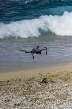 RC uzaktan kumandalı İHA deniz dalgalarının yakınındaki sahile iniyor. Taşınabilir helikopter aygıtı yaz tatilinde..