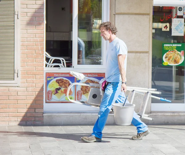 Handyman temizlik bir merdiven ve kova ve temizlik araçları ile sokakta yürüyor — Stok fotoğraf