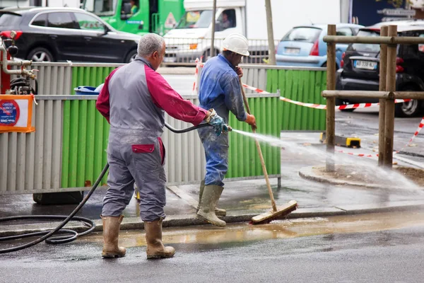 Limpeza de ruas por trabalhadores da construção civil que lavam com uma mangueira — Fotografia de Stock