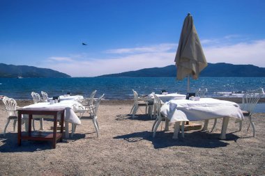 Akdeniz plajları turistleri, sahil kenarı tatil beldelerini, iklimsel sağlık merkezlerini bekliyor. Güneş pansiyonları, şezlonglar, şemsiyeler, yemek masaları ve plajdaki palmiye ağaçları, plaj tatil beldesi, paket tatil