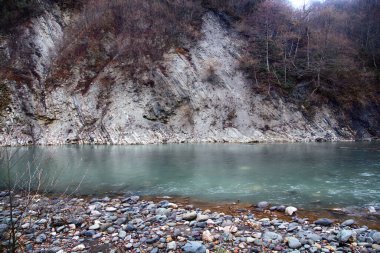 Dağ nehri kireçtaşı dağları boyunca akar, beyaz su. Kıyı kayaları ve demir çakıl taşları üzerindeki kireçtaşı tabakaları.