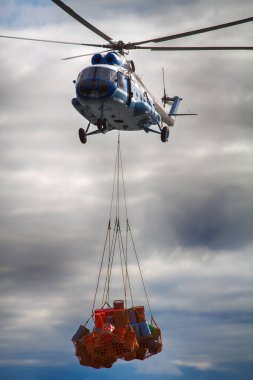 Hava kargo ve havacılık işleri, kargo hava servisi, kaldırma helikopteri. Helikopter boş metal varillerle askı (halat örgüsü) taşır