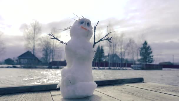 Snowman on the pier, opposite the open water and waves — Stock Video