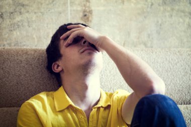 Evdeki koltukta oturan üzgün genç adamın tonlu fotoğrafı.