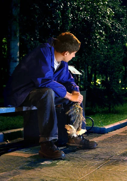 有花的年轻人坐在夜公园里 — 图库照片