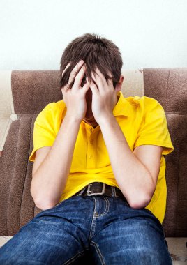 Odadaki koltukta oturan üzgün genç adam.