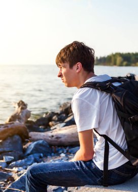 Deniz kenarında sırt çantası ile üzgün genç adam