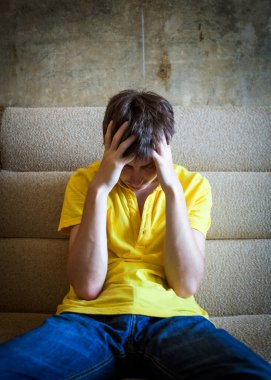 Evdeki kanepede oturan üzgün genç adam.