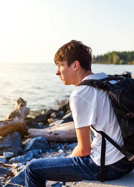 Deniz kenarında sırt çantası ile üzgün genç adam