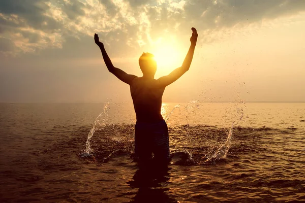 夕日の背景に水の水しぶきで幸せな男シルエットのトーン写真 — ストック写真