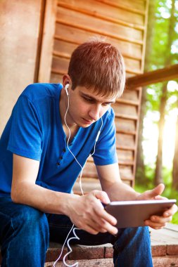 Genç adam bir Tablet bilgisayar ve kulaklık açık evin yanında