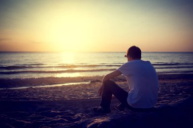 Tonda fotoğraf üzgün ve yalnız genç adam deniz kenarında oturup