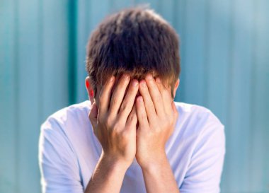 Toned Photo of Sad Teenager cover his Face on the Wall Background clipart