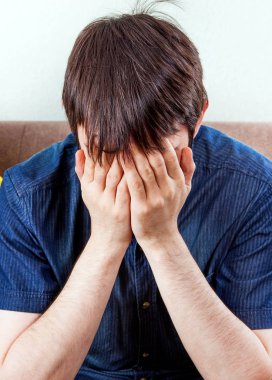 Evdeki kanepede oturan üzgün genç adam.