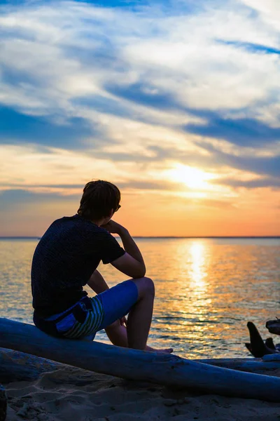 Jonge Man Zitten Een Logboek Het Overwegen Van Een Zonsondergang — Stockfoto