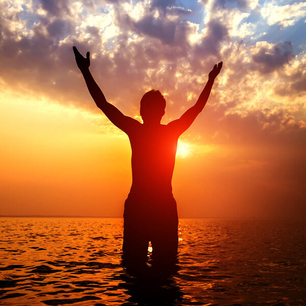 Toned Photo of Man Silhouette with Hands Up in the Water on the Sunset Background