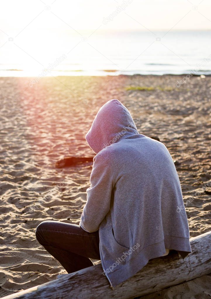 Sad and Lonely Man in a Hoodie sit on the Log at Seaside