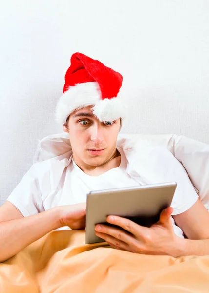 Verrast Jonge Man Kerstmuts Met Een Tabletcomputer Het Bed — Stockfoto