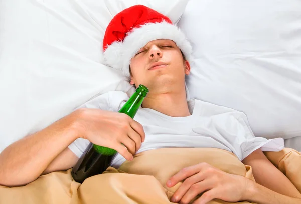 Молодой Человек Санта Шапке Спит Кровати Бутылкой Пива — стоковое фото