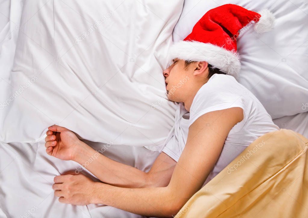 Tired Young Man in Santa Hat sleep in the Bed at the Home