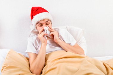 Noel Baba şapkası hasta genç adam yatakta bir mendil ile