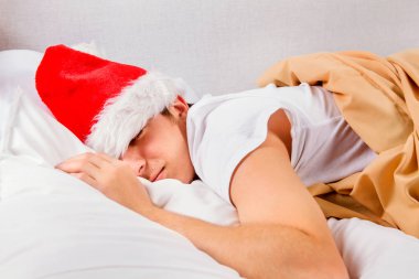 Genç adam Noel Baba şapkası uyurken evde yatakta yorgun