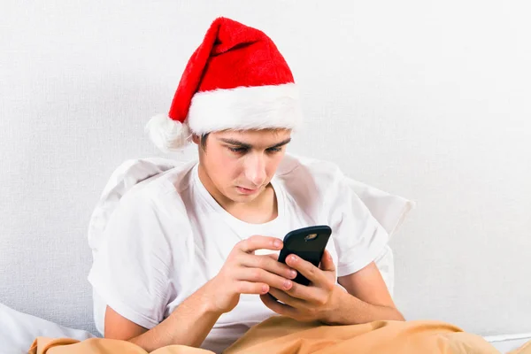 Trieste Jongeman Kerstmuts Met Een Telefoon Het Bed — Stockfoto