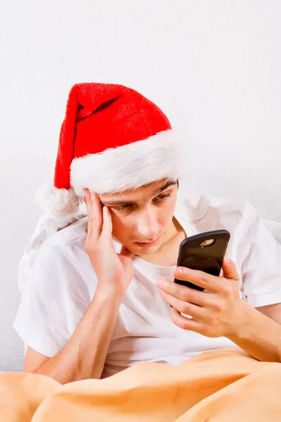 Θλιβερή Νεαρός Άνδρας Καπέλο Santa Ένα Τηλέφωνο Στο Κρεβάτι — Φωτογραφία Αρχείου