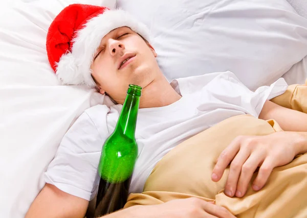 サンタの帽子で若い男がビール瓶でベッドで寝る — ストック写真