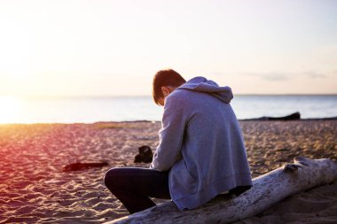 Üzgün ve yalnız genç adam deniz kenarında oturuyor.