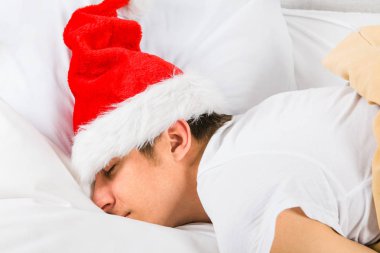 Genç adam Noel Baba şapkası uyurken evde yatakta yorgun