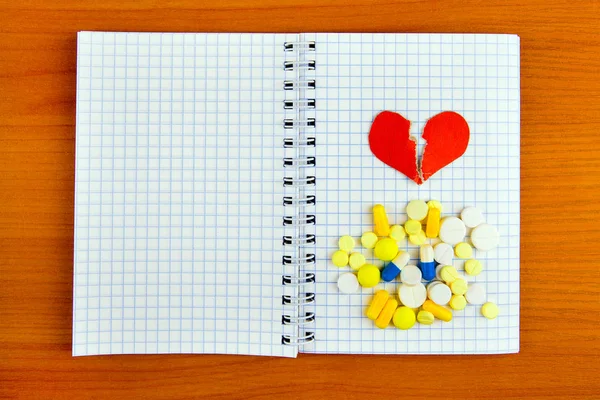 Empty Writing Pad with a Pills and Broken Red Heart Shape on the Wooden Table closeup