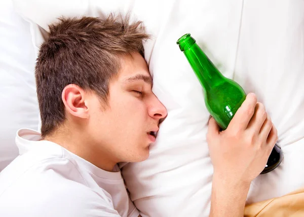 自宅でベッドでビール瓶を持つ若い男睡眠 — ストック写真