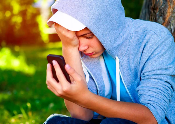 Sad Teenager with the Mobile Phone in the Summer Park