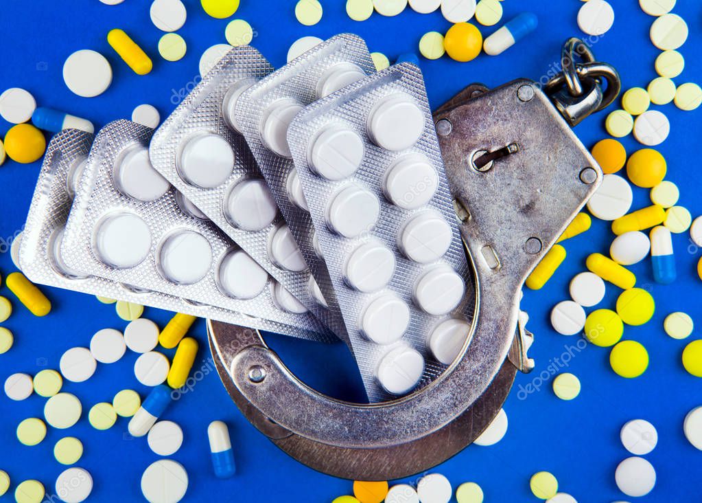 Scattering Pills with a Handcuffs on the Blue Paper Background closeup