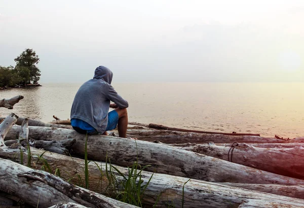 パーカーで孤独な若い男が海の背景の上に座る — ストック写真