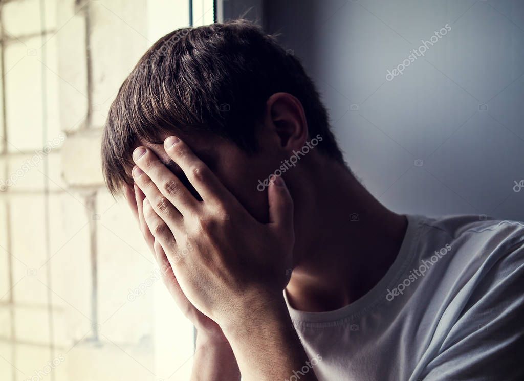 Sad Young Man hide a Face by the Window in the Room