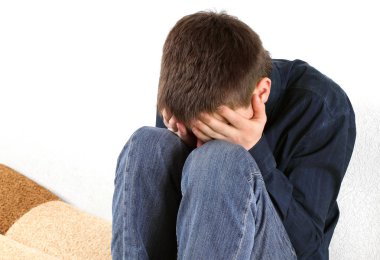 Evdeki kanepede oturan üzgün genç adam.