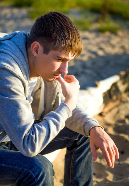 沉思的年轻人坐在自然背景的日志上 — 图库照片