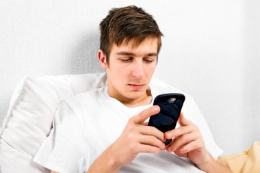 Evde yatakta bir telefon ile genç adam