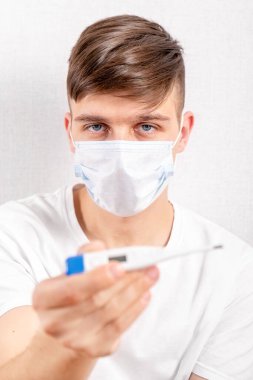 Grip Maskeli Genç Adam Odadaki Duvar 'ın yanında bir termometre gösteriyor.