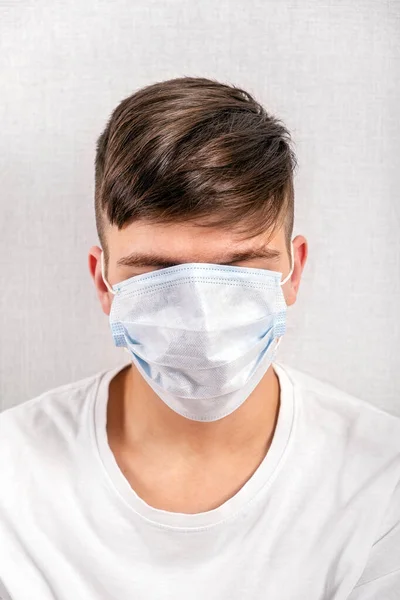 年轻人用白墙旁边的流感面具遮住自己的脸 — 图库照片