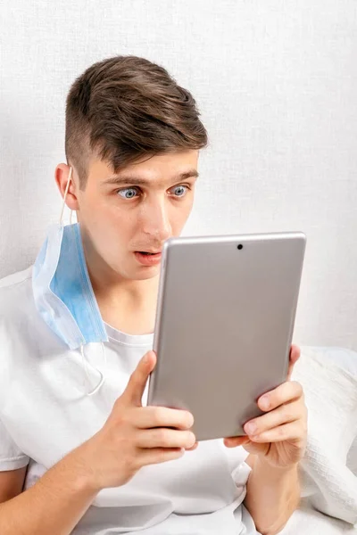 Verrast Jonge Man Met Een Griepmasker Met Een Tablet Aan — Stockfoto