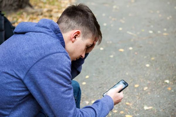 Telefonu Olan Dalgın Genç Adam Sonbahar Parkındaki Bankta Oturuyor — Stok fotoğraf