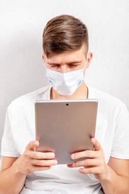 Grip Maskeli Genç Adam, duvarın yanında bir tabletle.