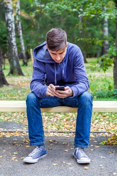 Jongeman Met Telefoon Zit Bank Het Herfstpark — Stockfoto