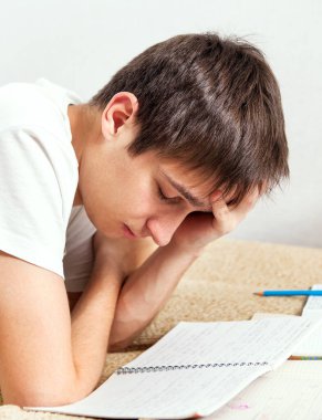 Yorgun öğrenci evdeki kanepede ödev yapıyor.