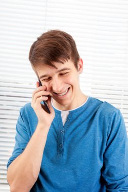 Jalousie 'nin arka planında cep telefonu olan mutlu genç adam.