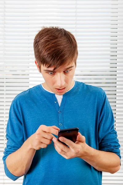 Überraschter Junger Mann Mit Handy Auf Dem Jalousie Hintergrund Einem — Stockfoto
